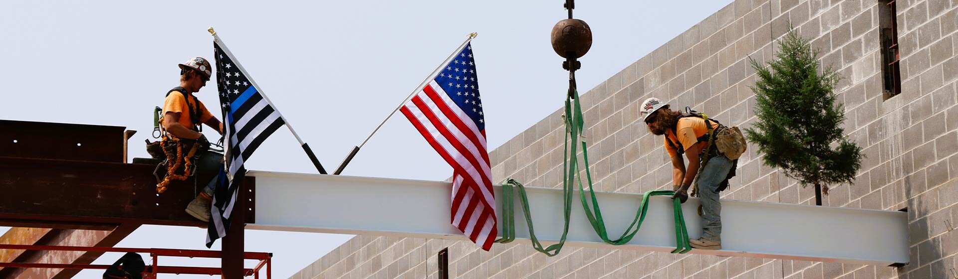 Two workers on a beam installing the American and Thin Blue Line flags. 